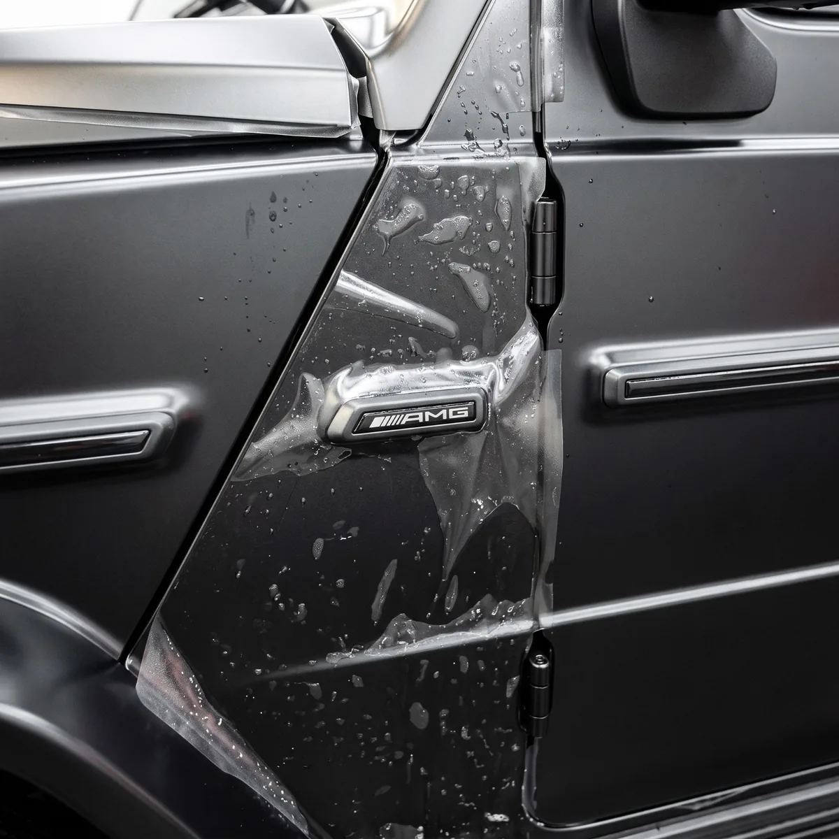 Clear paint protection film being applied over the AMG badge of a matte gray Mercedes G-Wagon