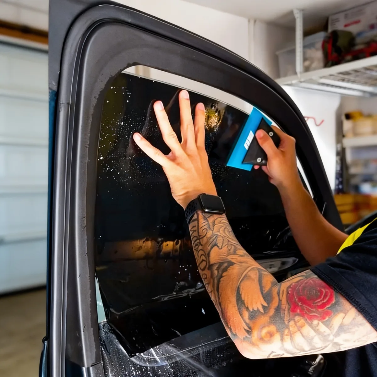 Installer squeegeeing window tint film onto a car door window